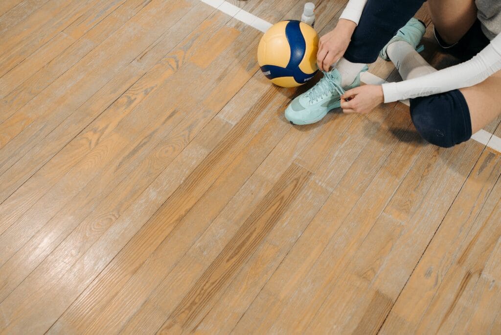 Person in Green Sneakers Sitting on Brown Wooden Floor